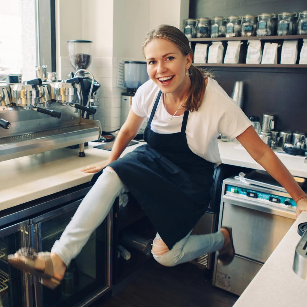 Young Caucasian barista laughing having fun jumping at work place. Small business concept