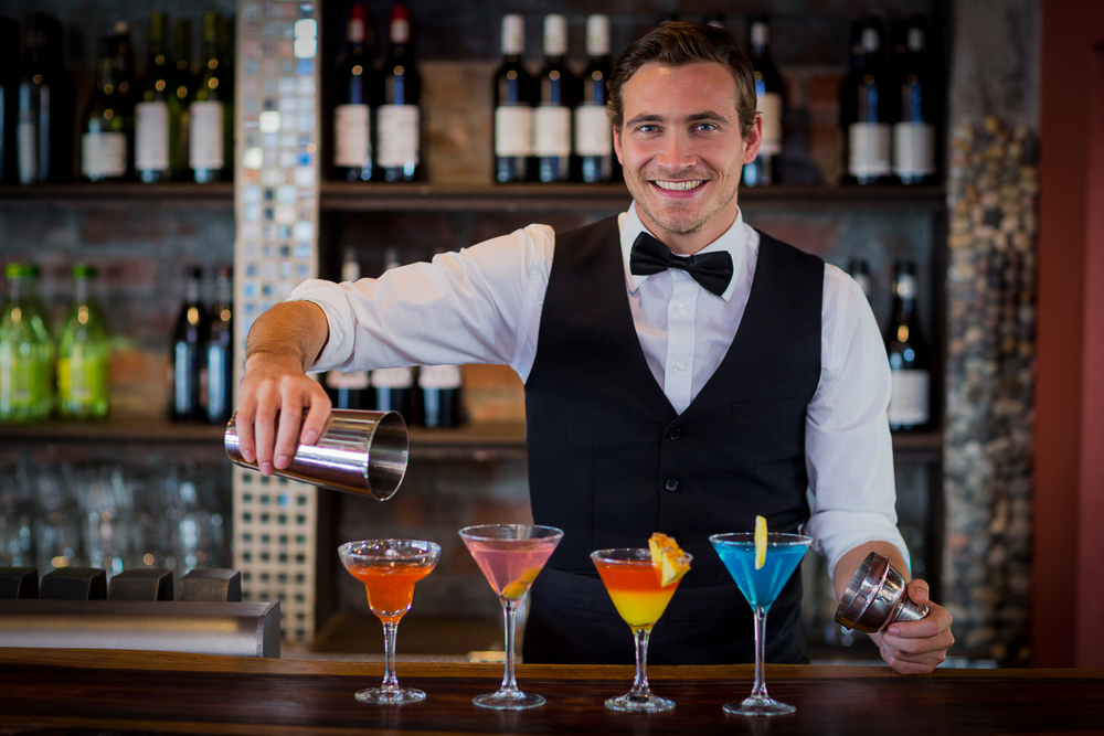 portrait of bartender pouring a orange martini drink in the glass at bar